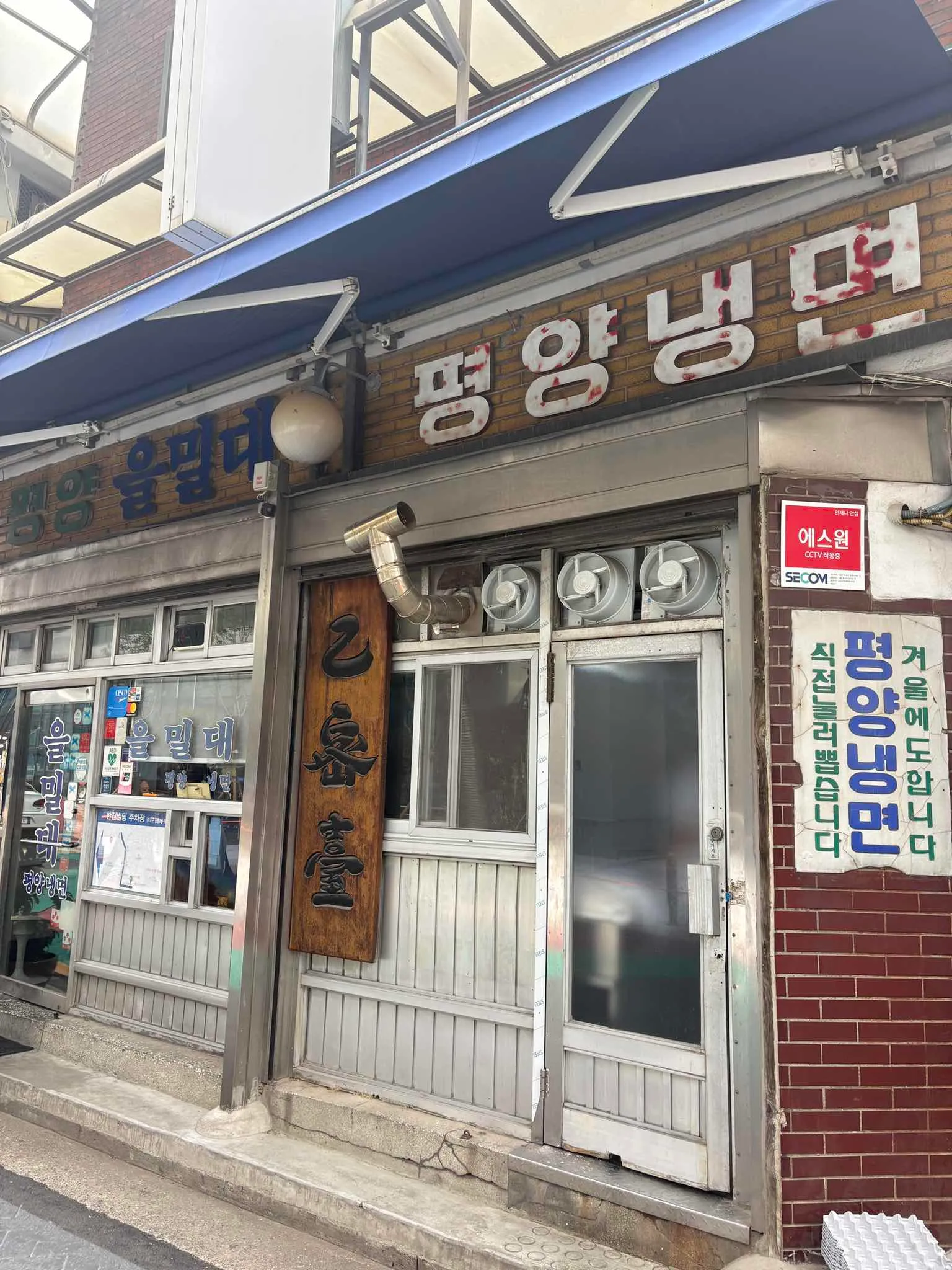 낡은 벽돌과 파란 차양, 평양냉면 간판이 보이는 을밀대 본점 입구