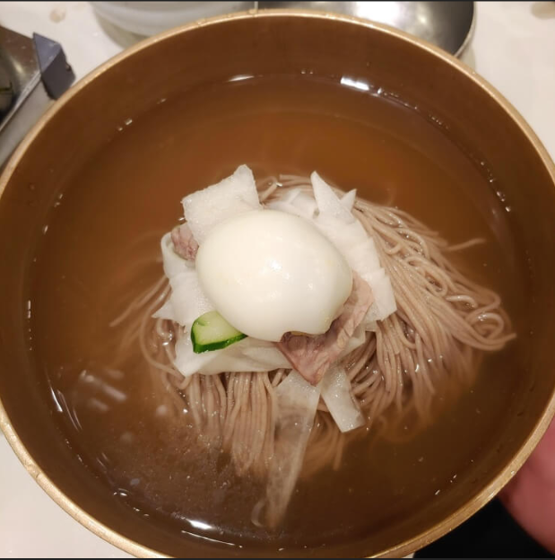 황동 그릇의 맑은 육수에 메밀 면과 고기, 무, 오이, 삶은 달걀을 올린 형제갈비 평양냉면