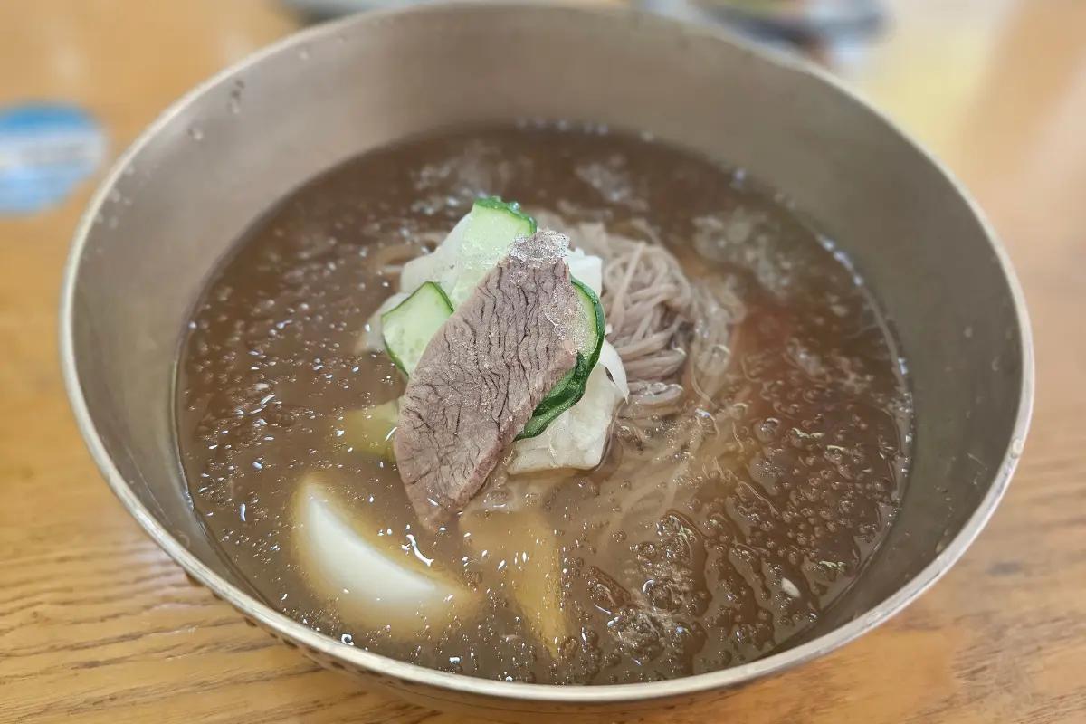 갈색빛 소고기 육수에 메밀 면과 고기, 오이, 무를 올린 미르밀옥류관 평양냉면