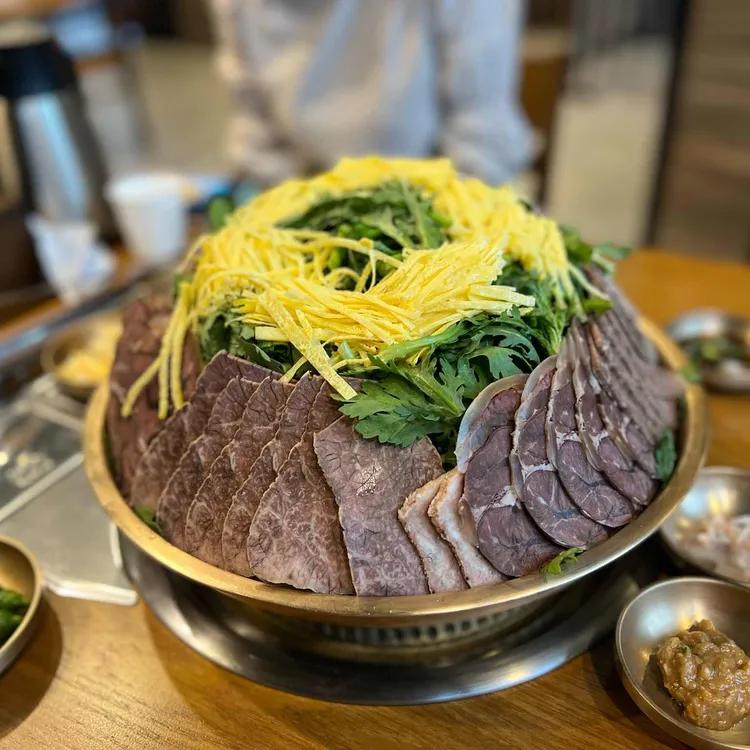 둥근 전골 그릇에 소고기와 쑥갓, 달걀지단을 풍성하게 담은 능라도 어복쟁반